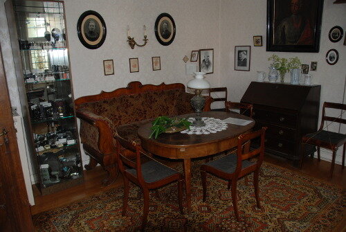 Rokoko-Zimmer: Weiße Tapeten mit Verzierungen, sowie braune Möbel und ein stilvoller Teppich mit Muster